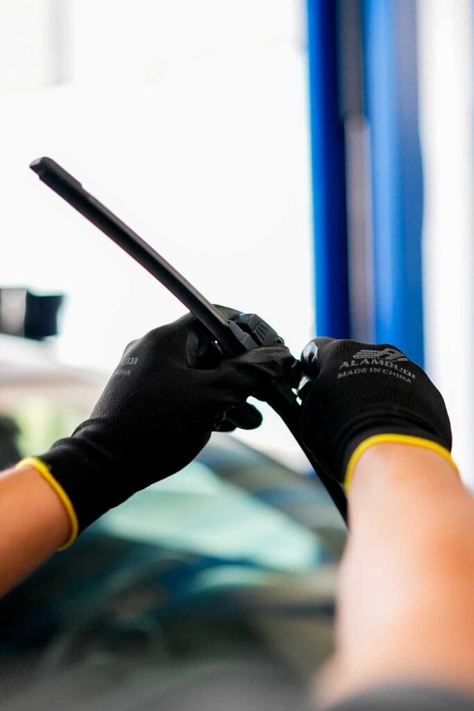 Mechanic wearing black gloves using a black plastic pry tool inside a car.