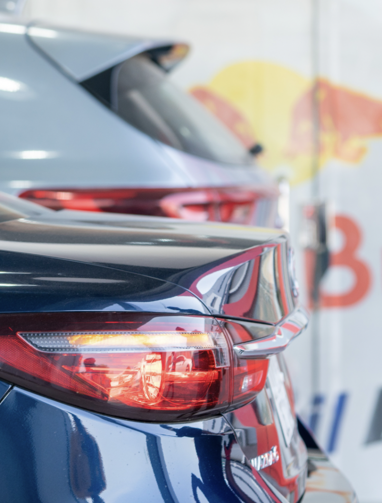 Close-up of a blue car's red tail light with other cars in a showroom background.