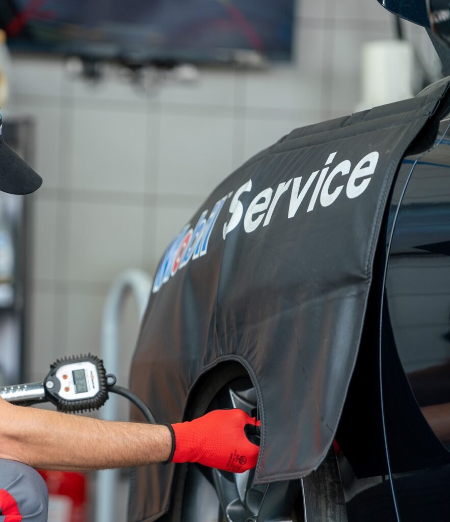 Close-up of a service van with bold 'Service' lettering and a mechanic wearing red gloves reaching toward the wheel, blurred workshop background.