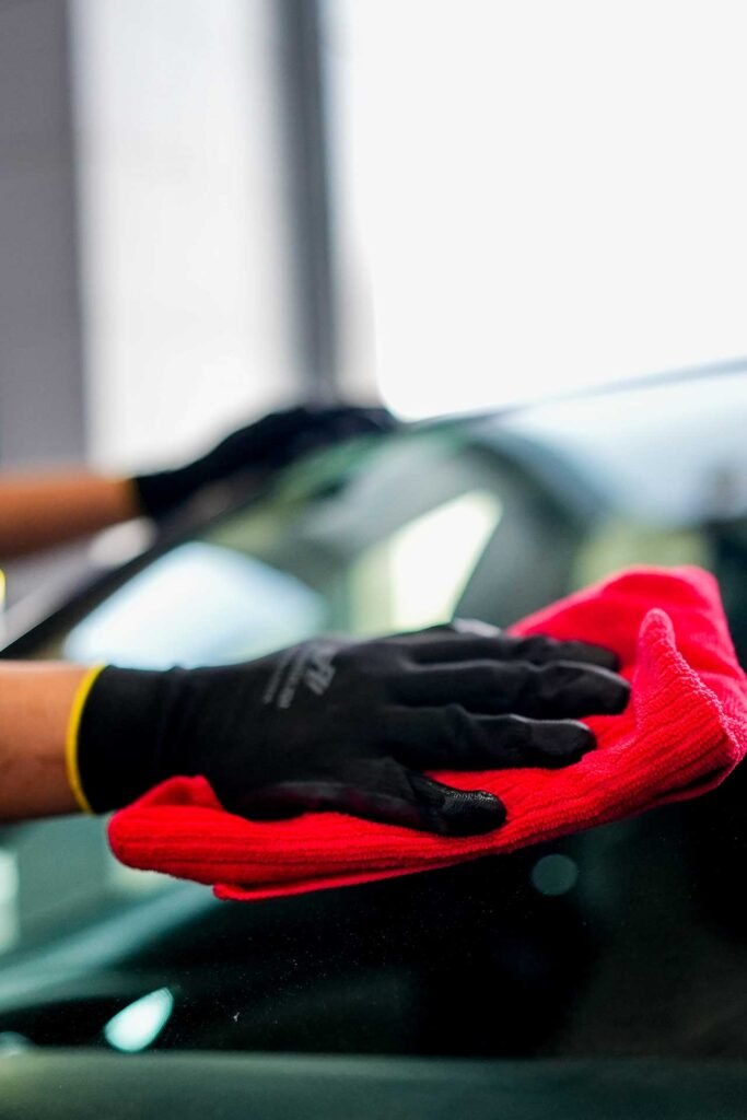 Gloved hands wiping a red towel across a car's dark, glossy surface.